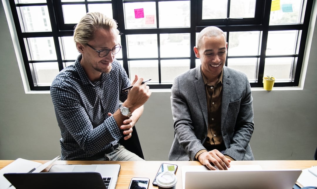 Two, professional men collaborating and working on laptops.